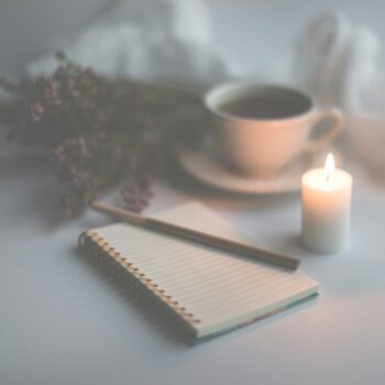 white candle on white ruled paper beside white ceramic mug