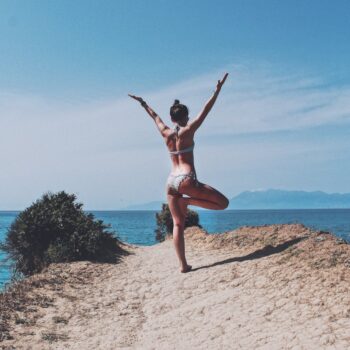 a woman in a bikini doing a yoga pose on a beach