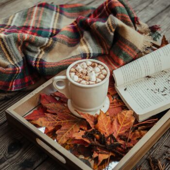 mug of coffee with marshmallow in front of open book on tray