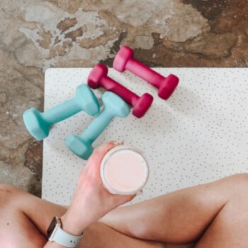 person holding white liquid filled cup above two pairs of dumbbells
